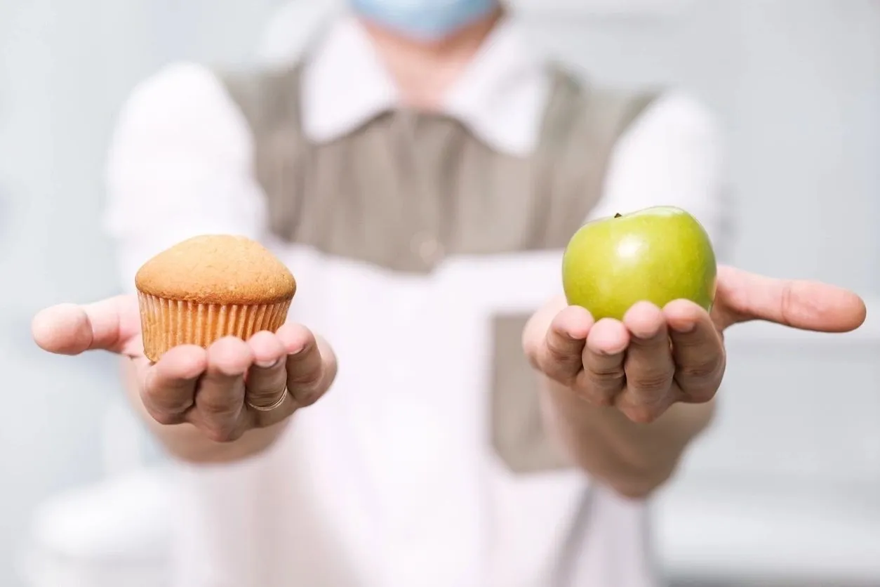 A person holding an apple and cupcake in their hands.