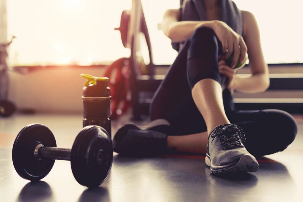 A person sitting on the ground with a bottle of water and a dumbbell.