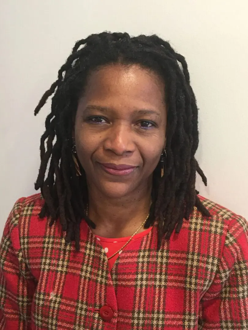 A woman with dreads in plaid shirt and red jacket.