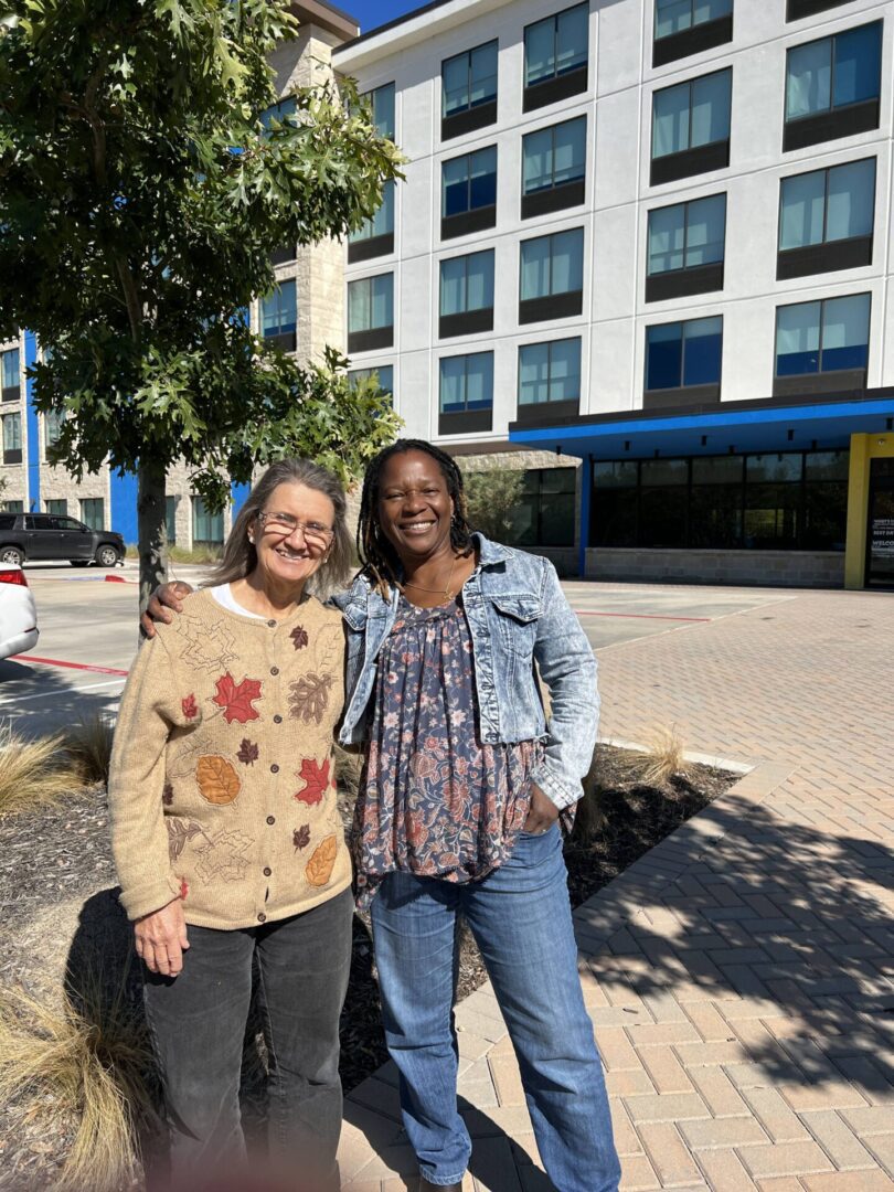 Two women standing next to each other on a sidewalk.